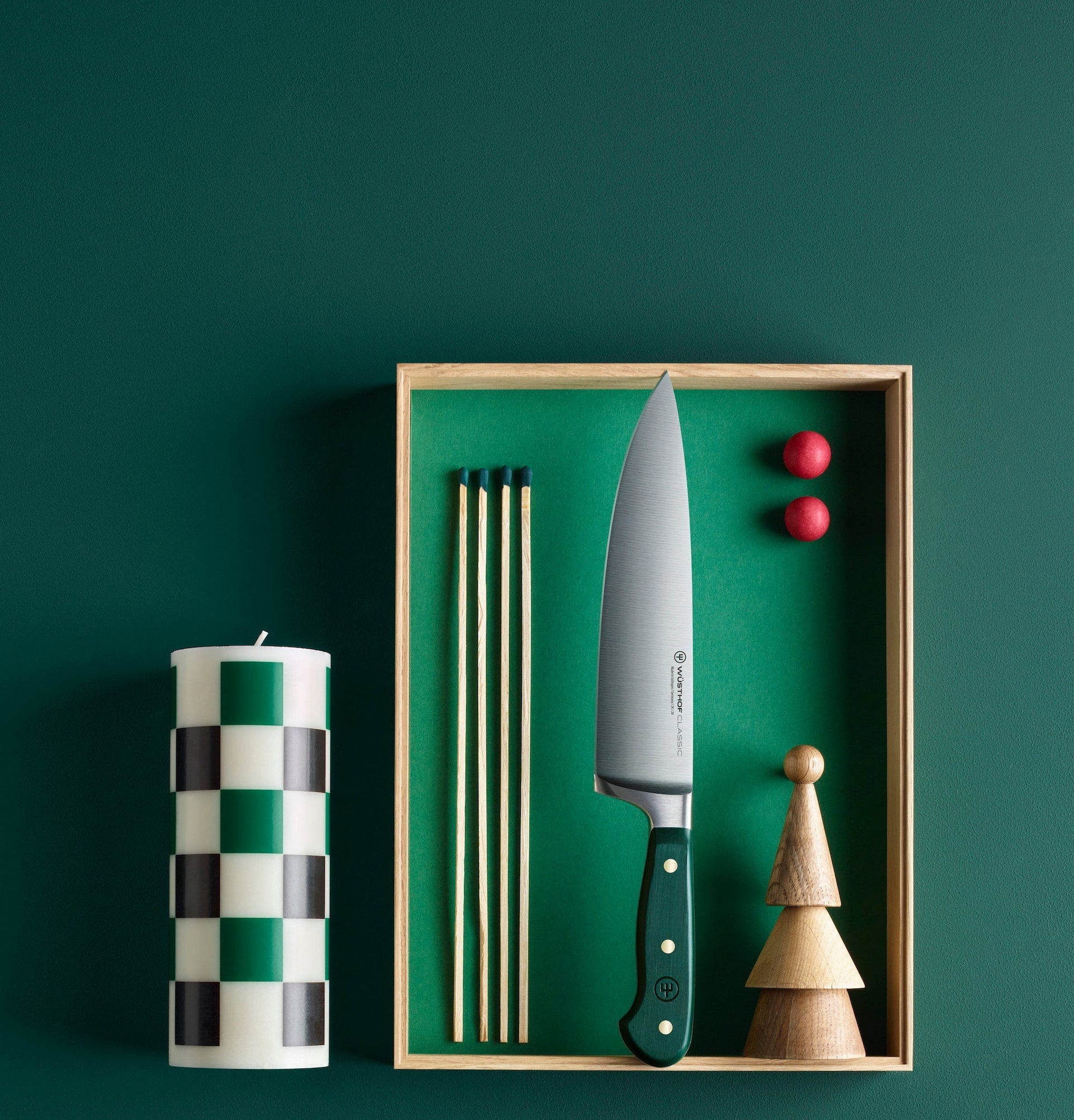 Kitchen knife with checkered candle and wooden tool in a box on a green background