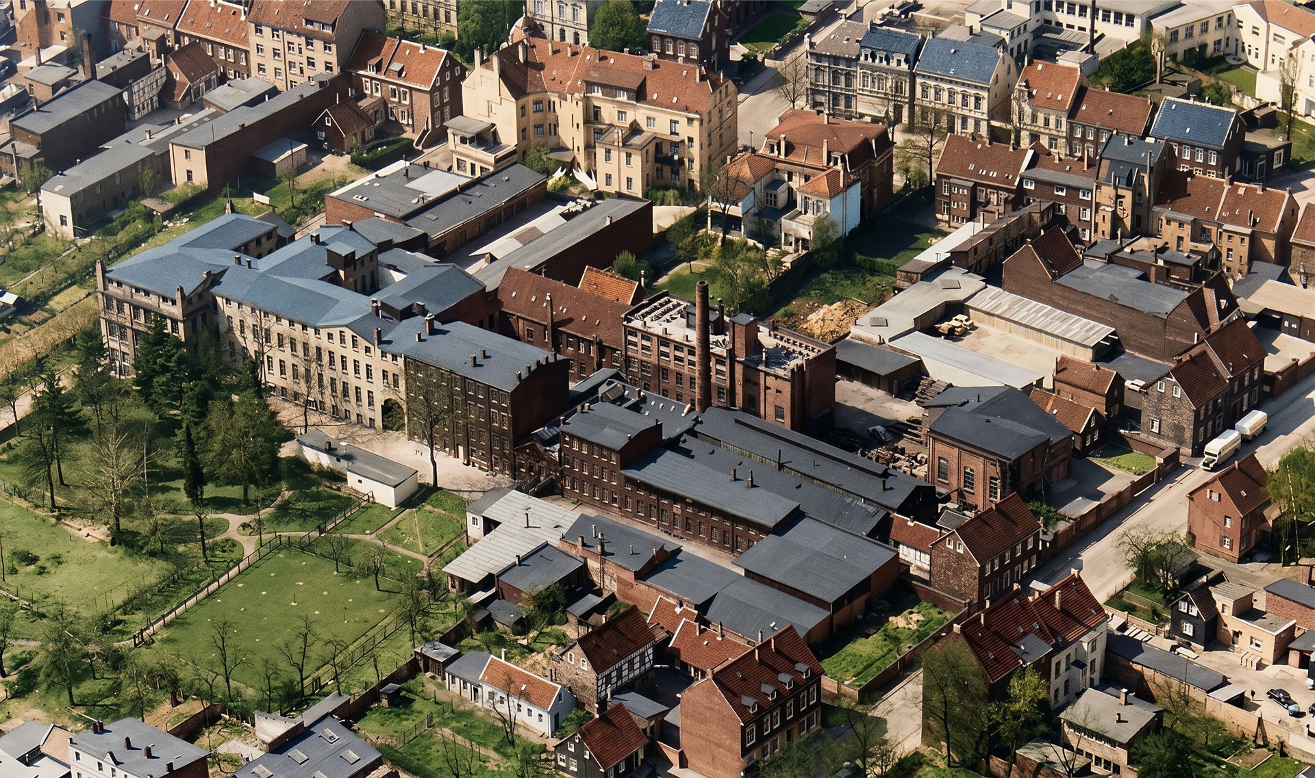 Aerial view of an urban area with densely packed brick buildings, streets, and patches of green spaces surrounding the neighborhood.