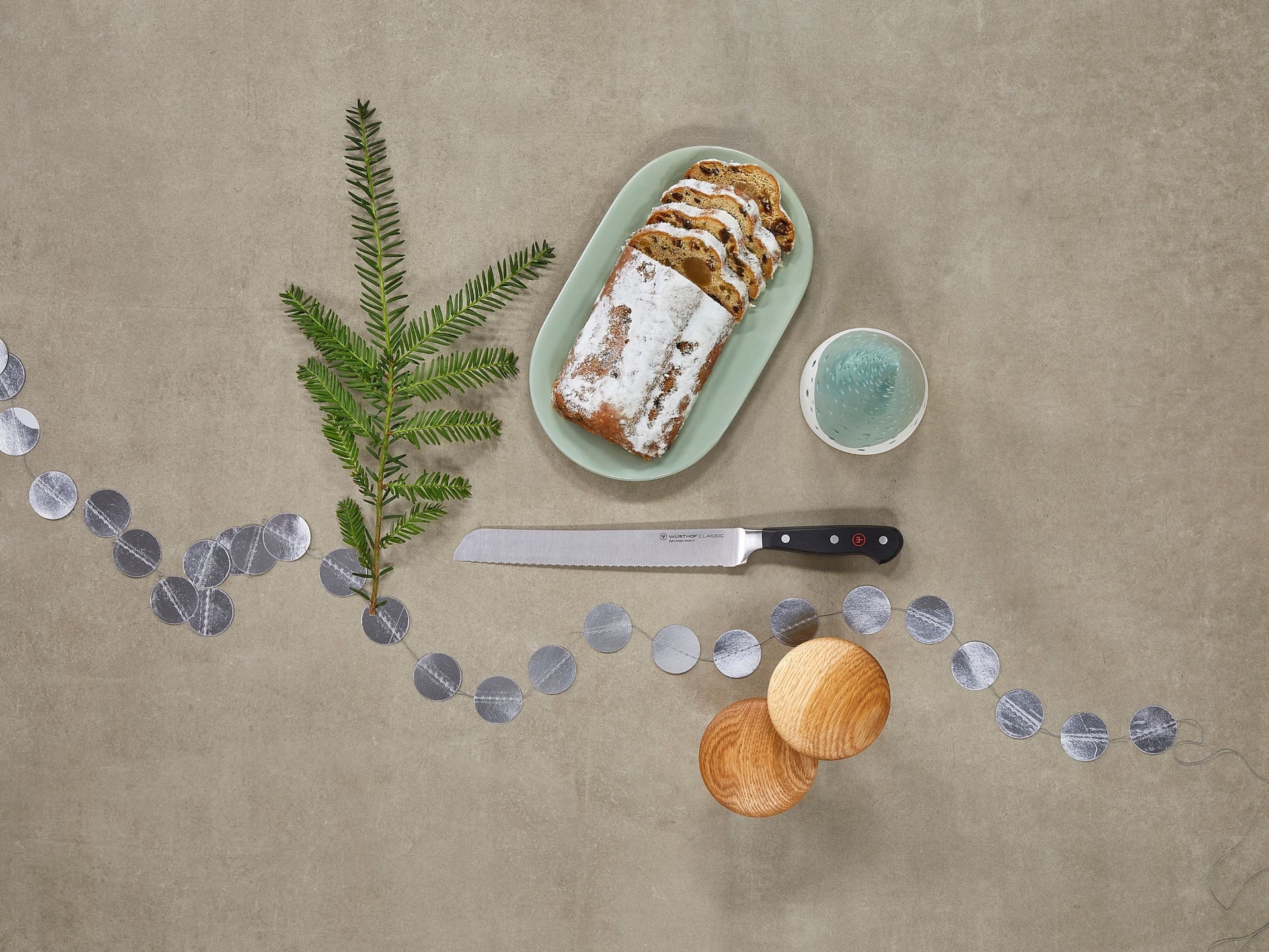Loaf of bread on a plate with a knife, small bowl, and decorative elements on a beige surface