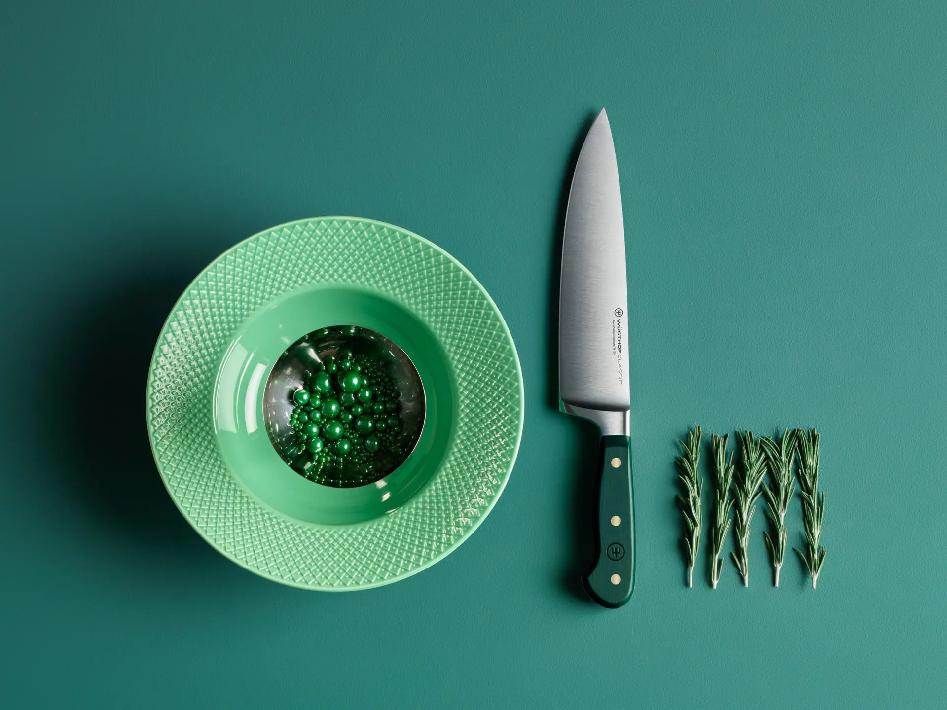 Green plate with a small dish, knife, and sprigs of rosemary on a green background