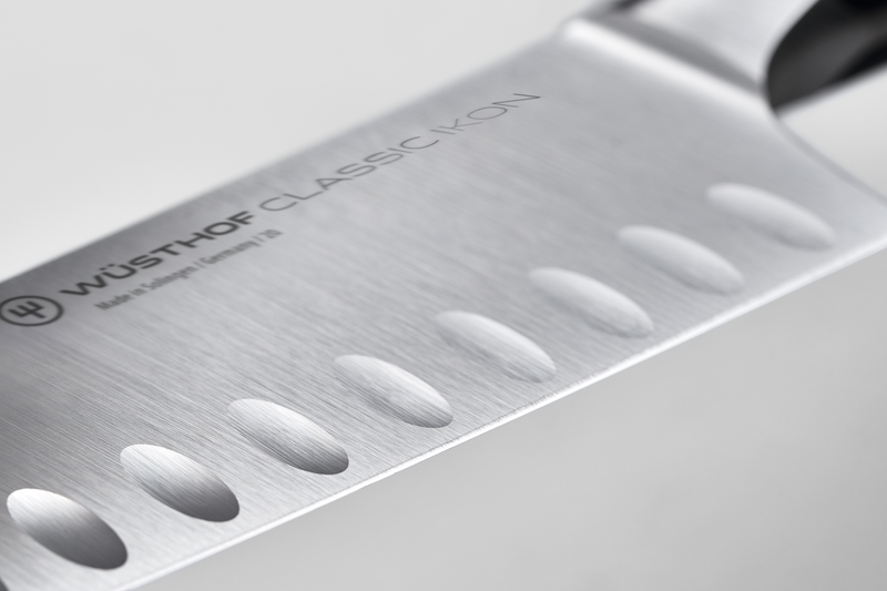 Close-up of a brushed stainless steel kitchen knife blade engraved with WÜSTHOF CLASSIC IKON branding and featuring oval air pockets along the edge.