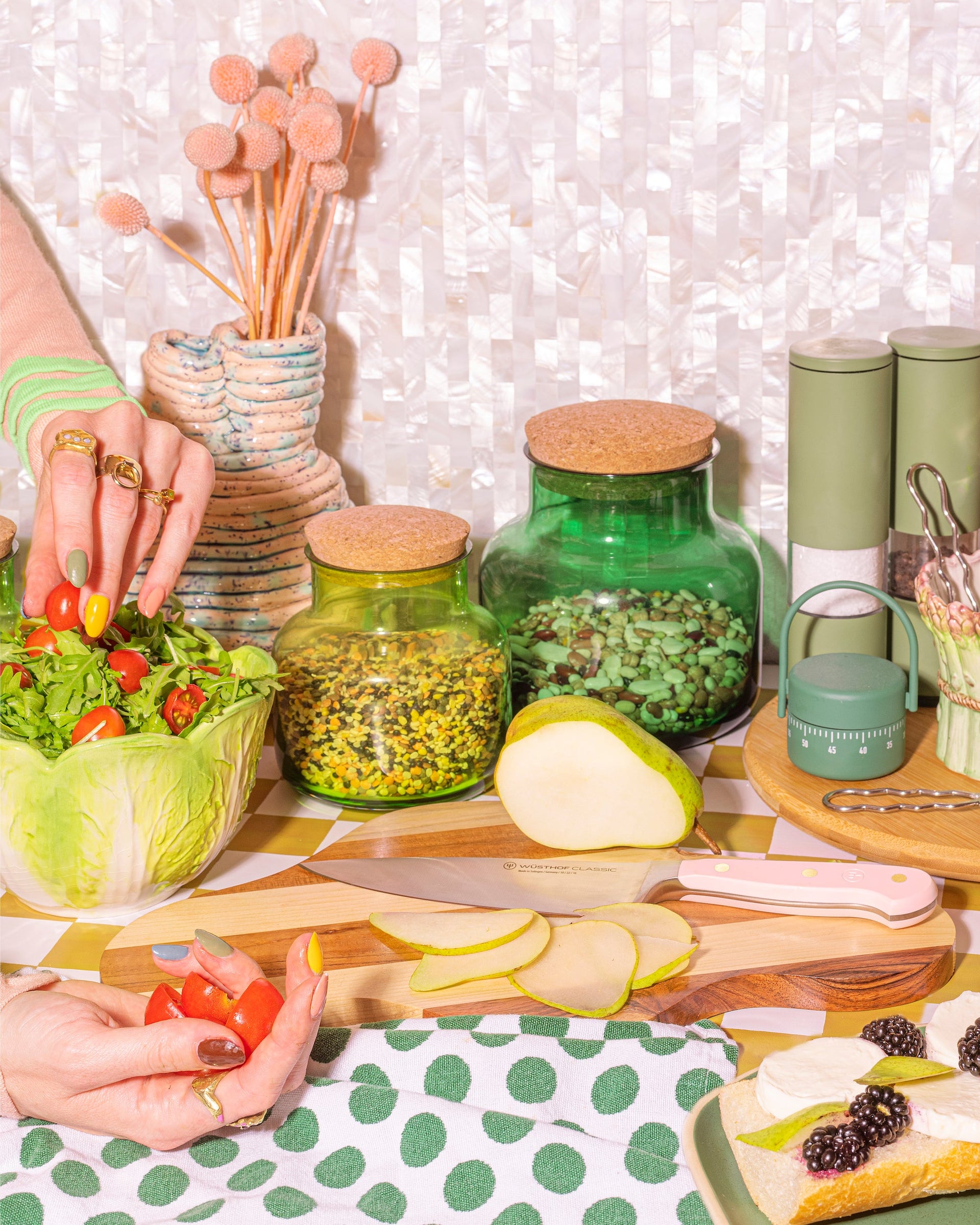 Table with food preparation items including a bowl of salad, apples, and jars on a polka dot tablecloth.