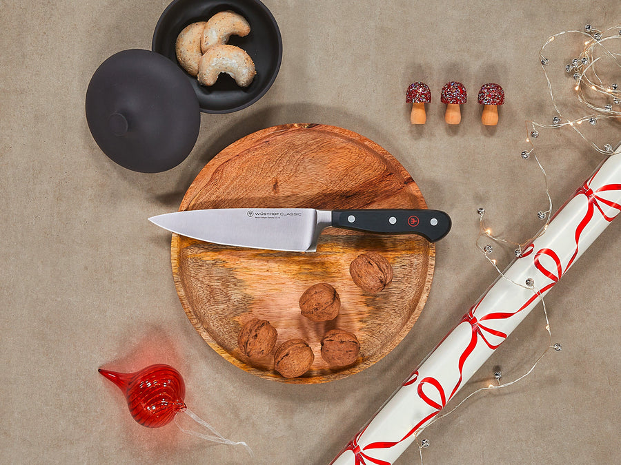 Wooden cutting board with knife, cashews, and decorative items on a beige surface