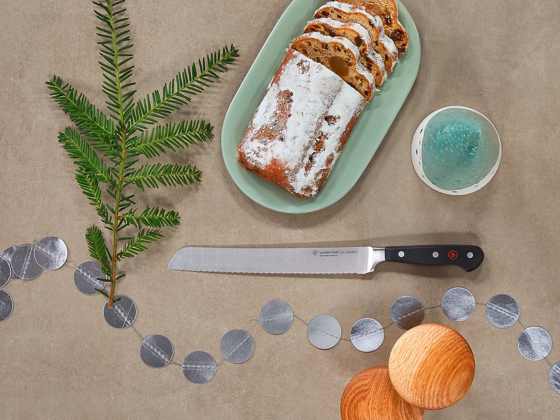 Loaf of bread with icing on a green plate, knife, and decorative elements on a beige surface